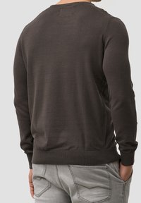 Brown long-sleeve sweater with ribbed cuff and hem, made from soft material, worn with light gray jeans featuring double back pockets.