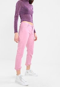 Vaqueros de denim rosa con dobladillos desflecados, combinados con una camiseta de manga larga ajustada de color púrpura y zapatillas blancas. La tela tiene un ligero brillo.