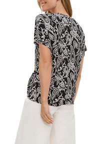 Zwart-wit korte mouwen top met paisley patroon, lichte stof, ontspannen pasvorm en ronde zoom, gecombineerd met lichte brede pijpen.