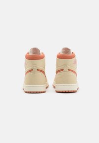 Wysokie sneakersy w beżowym zamszu z koralowymi akcentami, z teksturowaną powierzchnią, wyściełanymi kołnierzami i białą podeszwą z różowawą gumą.