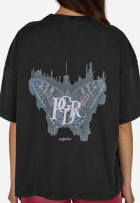 T-shirt oversized preta com uma gráfica colorida de borboleta e texto estilizado. Tecido macio com um ajuste solto, mangas curtas.