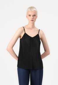 Μαύρο πλισέ μπλουζάκι με λεπτές τιράντες και V-λυγισμένο λαιμό. Το ύφασμα έχει λεία υφή και πέφτει χαλαρά, συνδυασμένο με μπλε τζην παντελόνι.