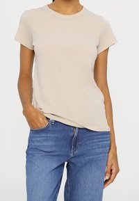 Beige T-shirt met korte mouwen van zachte stof, met een ronde halslijn en een ontspannen pasvorm, gecombineerd met blauwe spijkerbroek.