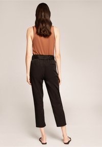 Brun ärmlös topp kombinerad med svarta högmidjade byxor, med ett snitt som betonar midjan och en kortad ben-design. Slät textur med minimal detaljering.