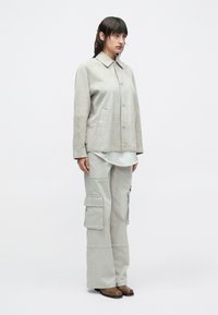 Hellgraue Wildlederjacke mit Kragen und Fronttaschen, kombiniert mit hellgrauen Cargohosen mit mehreren Taschen und lockerem Schnitt.