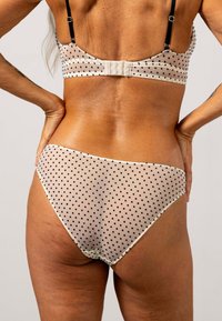 Beige polka dot bralette en bijbehorende bikini, met zwarte stippen, verstelbare bandjes en een haak-en-oog sluiting aan de achterkant. Glad textuur.