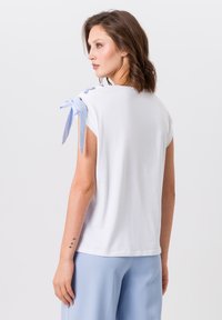 Witte korte mouwen t-shirt met blauwe gestreepte strikjes op de schouders, voorzien van een ronde halslijn en een losse pasvorm, gedragen met lichtblauwe broek.