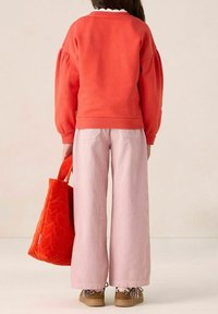 Sweatshirt rouge à manches bouffantes, pantalon large en velours côtelé rose clair et sac fourre-tout matelassé orange. Chaussures à motif léopard.