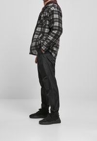 Veste en flanelle à carreaux noirs et gris, manches longues avec poches, associée à un pantalon noir effilé et des baskets de sport noires.