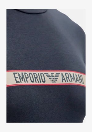 Sudadera azul marino con una prominente franja blanca y roja etiquetada "EMPORIO ARMANI" con un logo. La tela parece suave y ligeramente texturizada.