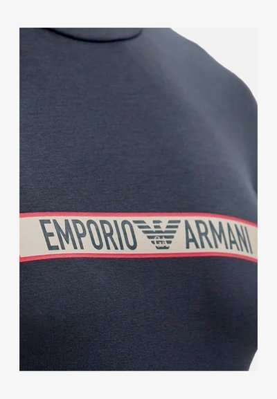 Felpa blu navy con una prominente striscia bianca e rossa contrassegnata "EMPORIO ARMANI" con un logo. Il tessuto appare liscio e leggermente testurizzato.