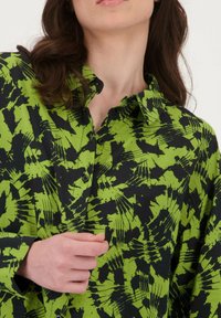 Groen en zwart overhemdd shirt met een gedurfde, abstracte print, voorzien van een klassieke kraag en een relaxte pasvorm. Textuur van de stof zichtbaar.