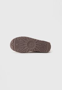 Semelle de chaussure en caoutchouc marron avec un motif texturé comportant des formes géométriques et un détail de logo circulaire au centre.