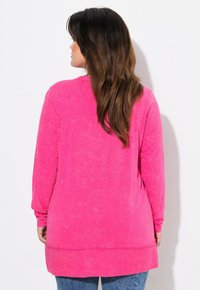 Top a maniche lunghe di un brillante colore rosa, con una vestibilità ampia e un tessuto testurizzato. L'orlo è leggermente più lungo sul retro per un look moderno.