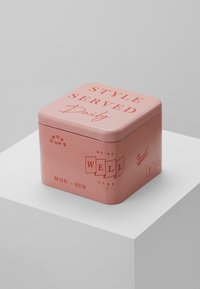 Boîte en métal rose carré avec des bords arrondis, comportant des textes graphiques en rouge et blanc. Les motifs incluent les jours de la semaine et des phrases.