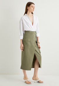 Chemise blanche à manches retroussées associée à une jupe enveloppante olive taille haute avec une fente sur le côté et des poches plaquées.