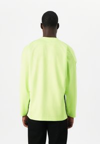 Majica z dolgimi rokavi iz svetlo neon zelenega mrežastega materiala, z bočnimi razporki, okroglim izrezom in sproščenim krojem.