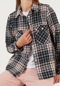 Camicia a quadri realizzata in morbido tessuto, con colori rosa, blu navy e nero. Dettagli significativi includono chiusure con bottoni e due tasche frontali.