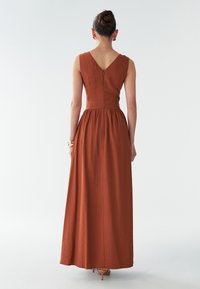 Maxi šaty z hrdzavej tkaniny s priliehavým korzetom, V-členíčkou na chrbte a nariaseným pásom. Obsahuje skrytý zips na chrbte.