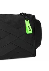 Bolsa de tela negra con tiras cruzadas. Presenta una etiqueta de tirador de cremallera verde y un logo. Forma rectangular con una superficie texturizada.