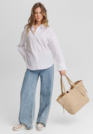 Weißes Hemd mit Knöpfen, hellblaue weite Jeans, beiger Wildleder-Umhängetasche mit Riemen und Sneaker mit beigen und grauen Akzenten.