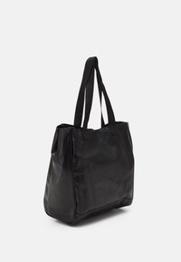 Sac fourre-tout noir large avec deux longues poignées et une surface lisse, légèrement brillante, incliné sur fond blanc.