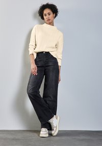 Krämfärgad ribbad tröja, högmidjade svarta vida jeans och beigefärgade sneakers med vita detaljer, mot en ljusgrå bakgrund.