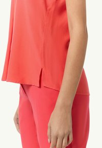 Koronkowa bluzka z krótkim rękawem, wykonana z lekkiego materiału o lekko luźnym kroju. Posiada rozcięte brzegi i gładką fakturę. Zestawiona z pasującymi spodniami.