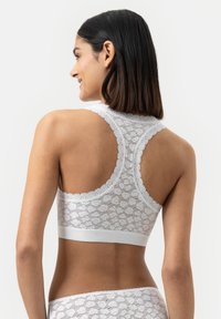 Weißes Spitzen-Bralette mit Racerback-Design, das mit gewellten Kanten und einem glatten Bund versehen ist. Intrikates Spitzenmuster und weiche Textur.