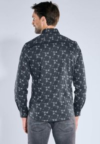 Hemd zum Zumknöpfen aus dunkelgrauem Stoff mit einem wiederholten Muster aus hellgrauen Vögeln; verfügt über lange Ärmel und einen spitzen Kragen.