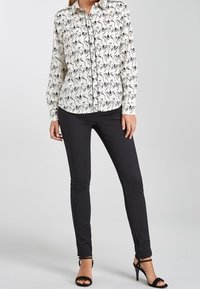 Chemise blanche à boutons avec un motif abstrait noir, pantalon noir slim-fit et escarpins noirs à brides ; tissu lisse et coupe ajustée.