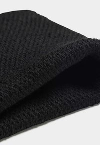 Melnā auduma ar teksturētu virsmu, salocīts, lai parādītu tā austu rakstu un mīksto, biezo audumu. Nav redzamu akcentu vai aparatūras.