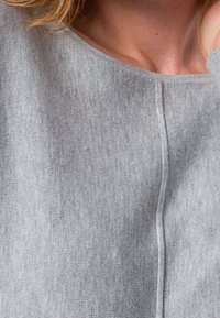Pull en tricot gris avec une texture douce, doté d'un large décolleté et d'une couture au centre pour le détail.