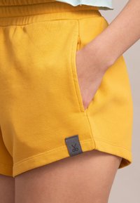 Geel korte broek van een katoenen mixstof met een gladde textuur, voorzien van zijzakken en een klein grijs logo-label op de zoom.