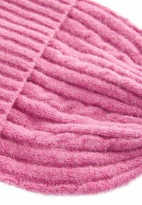 Roze gebreide beanie met een geribbelde textuur, voorzien van een zachte, pluizige afwerking en variërende dikte in de stof voor extra dimensie.