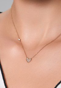 Złota naszyjnik z sercowym wisiorkiem ozdobionym przezroczystymi cyrkoniami, na cienkim łańcuszku, z małym okrągłym akcentem przy zapięciu.
