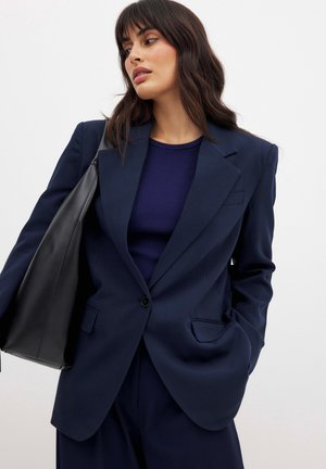 Navy blue blazer made of smooth fabric, featuring a single button closure, notched lapels, and two angled front pockets.