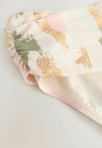 Badkläder med en mörk midja, tillverkade av mjukt tyg. Mönster i rosa, guld och grönt på en krämfärgad bakgrund. Slät textur.