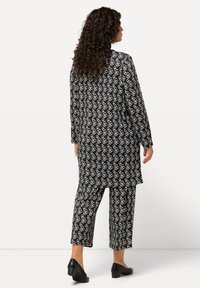 Conjunto de patrones en blanco y negro que incluye una chaqueta larga y pantalones a juego. La tela parece suave y tiene un corte holgado; unos zapatos texturizados completan el look.