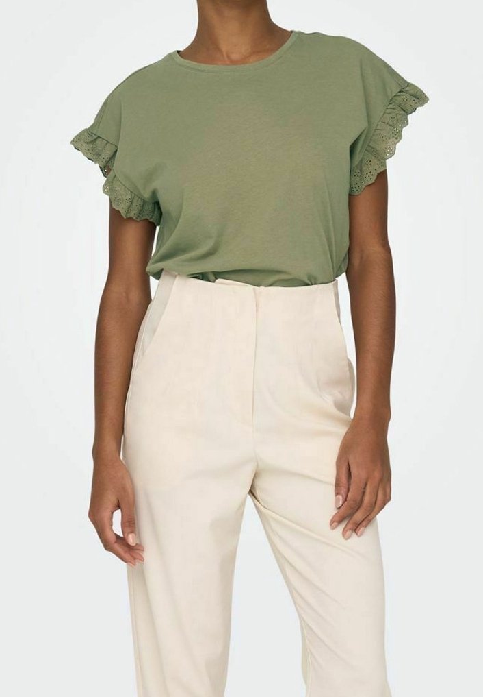 Olivegrön t-shirt med kort ärm och spetsdetaljer på ärmarna, ihop med högmidjade krämfärgade byxor. Slätt tyg, avslappnad passform.