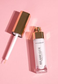 Clear lash glue in a rectangular glass bottle with a white applicator. The cap features a shiny gold finish. Text label reads "AYLASH GLUE."
