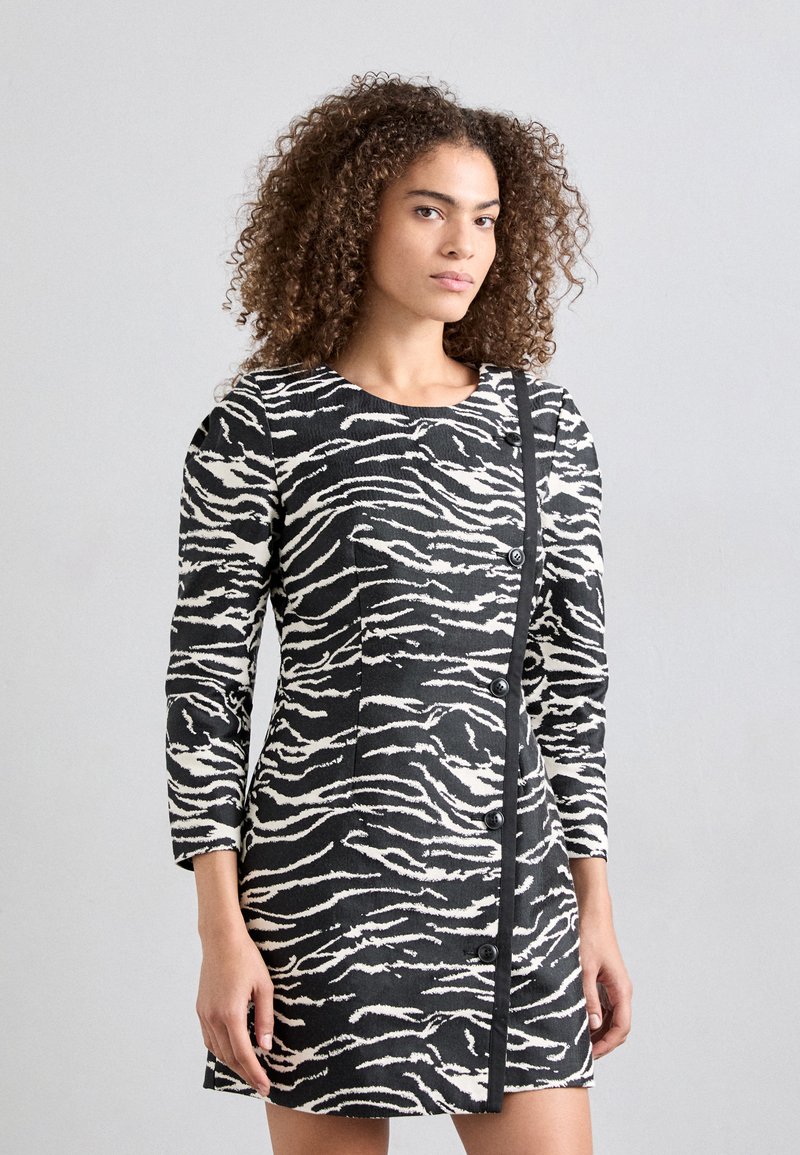 Black and white zebra-striped dress with long sleeves, round neckline, and a button closure along the side. Textured fabric with a fitted design.