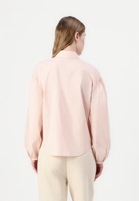 Light pink, long-sleeve shirt with a classic collar, gathered sleeves, and a rounded hem, made from soft-textured fabric.