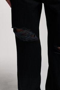 Black denim pants featuring prominent distressed rips at the knees, with frayed edges and a relaxed fit. Smooth texture with sturdy seams.