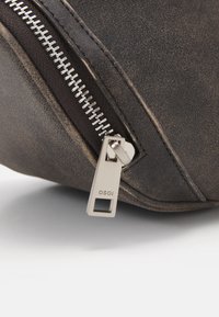 Custodia con zip in pelle marrone con un tirazip in metallo argentato con un foro rettangolare, superficie testurizzata e dettagli di cucitura visibili.