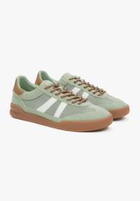 Zielone siatkowe sneakersy z białymi paskami, brązowymi sznurówkami i gumową podeszwą, łączą w sobie zamsz i oddychający materiał.