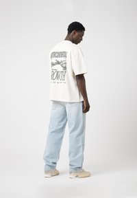 Cream graphic t-shirt with "INTERCONTINENTAL GROWTH" print on the back, paired with light blue baggy jeans and beige sneakers.