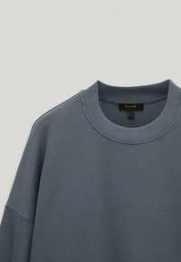 Grey sweatshirt with a round neckline and dropped shoulders, featuring a smooth texture and minimal stitching details.