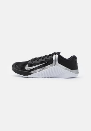 Schwarz-weißer Nike Sportschuh mit Mesh-Obermaterial, geometrischen Mustern, verstärkter Ferse und profilierter Sohle vor schlicht weißem Hintergrund.