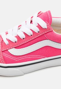 Růžové nízké tenisky s bílými tkaničkami, bílým vlnitým pruhem po straně, bílou podrážkou s černým okrajem a růžovým textilním svrškem.